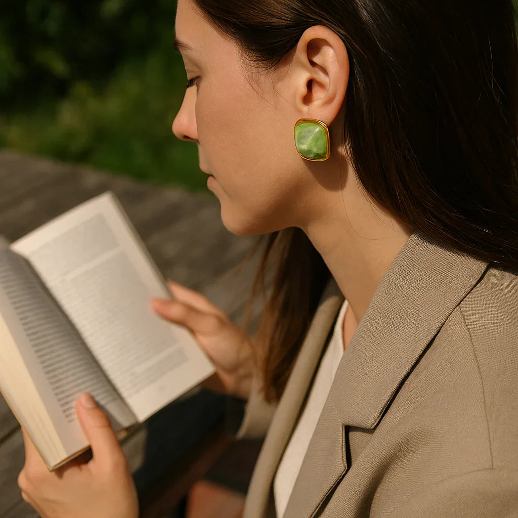 Woman in beige blazer reading a book outdoors, wearing a large green statement earring
