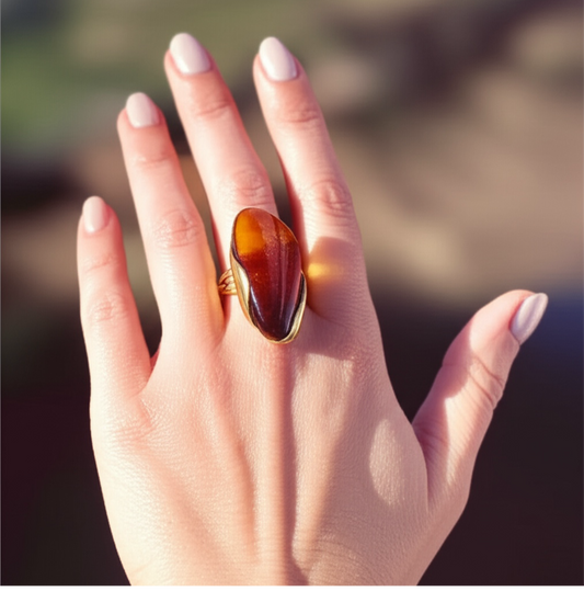 Hand wearing large amber gemstone statement ring with gold band, natural outdoor lighting