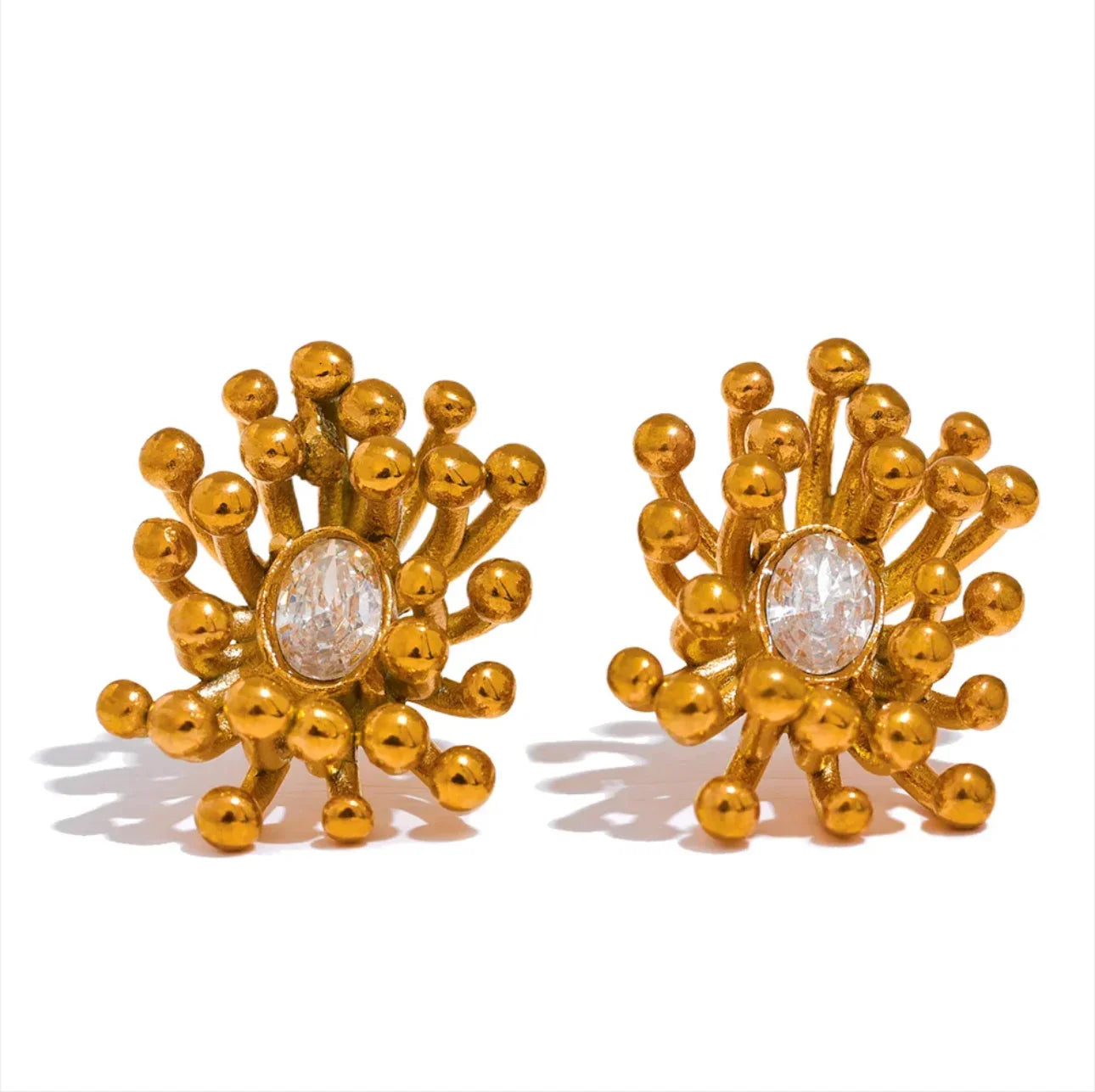 Gold statement earrings with round ball accents and central oval crystal on white background