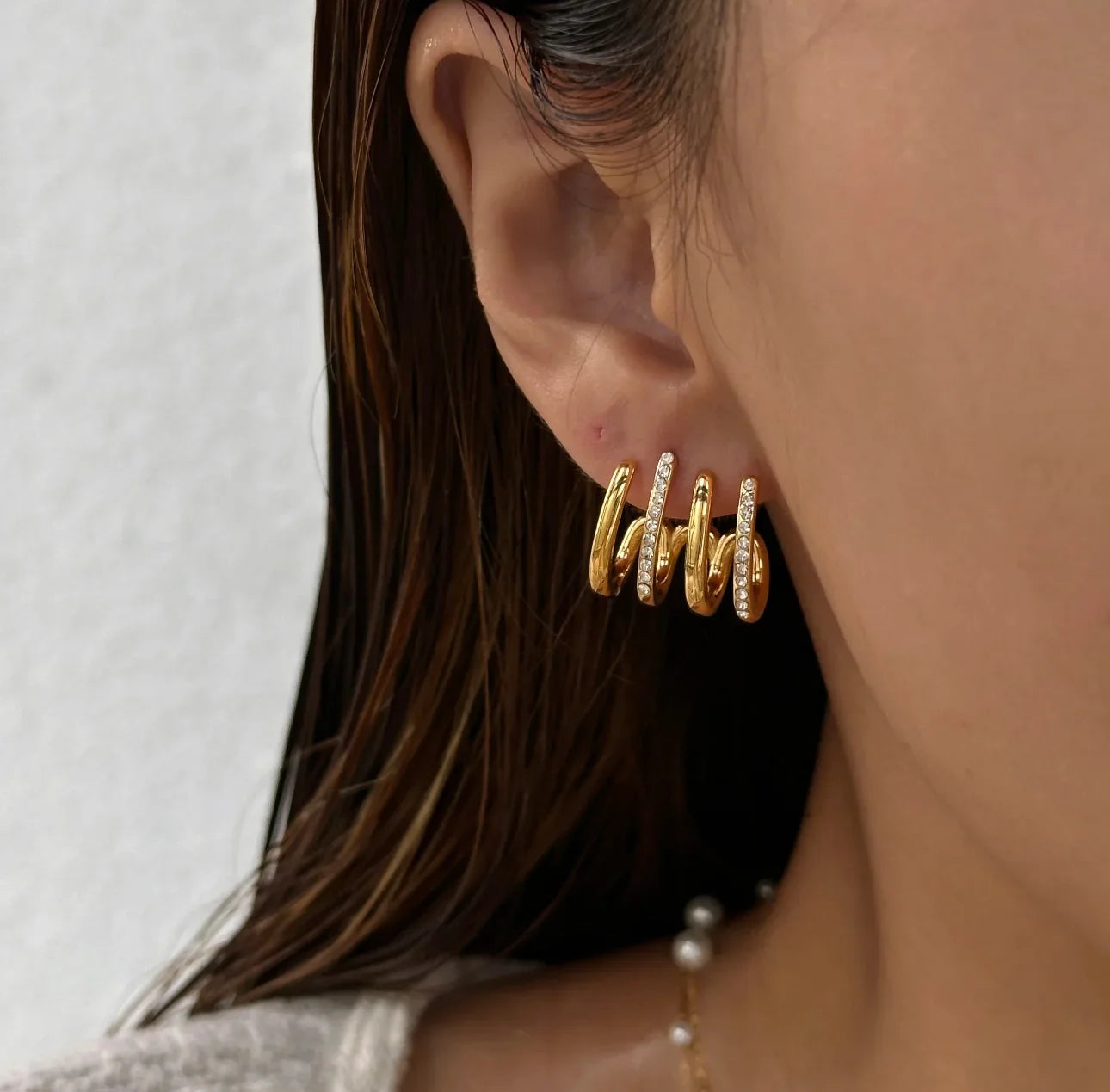 Gold spiral hoop earrings with crystal accents worn on ear, close-up jewelry photo