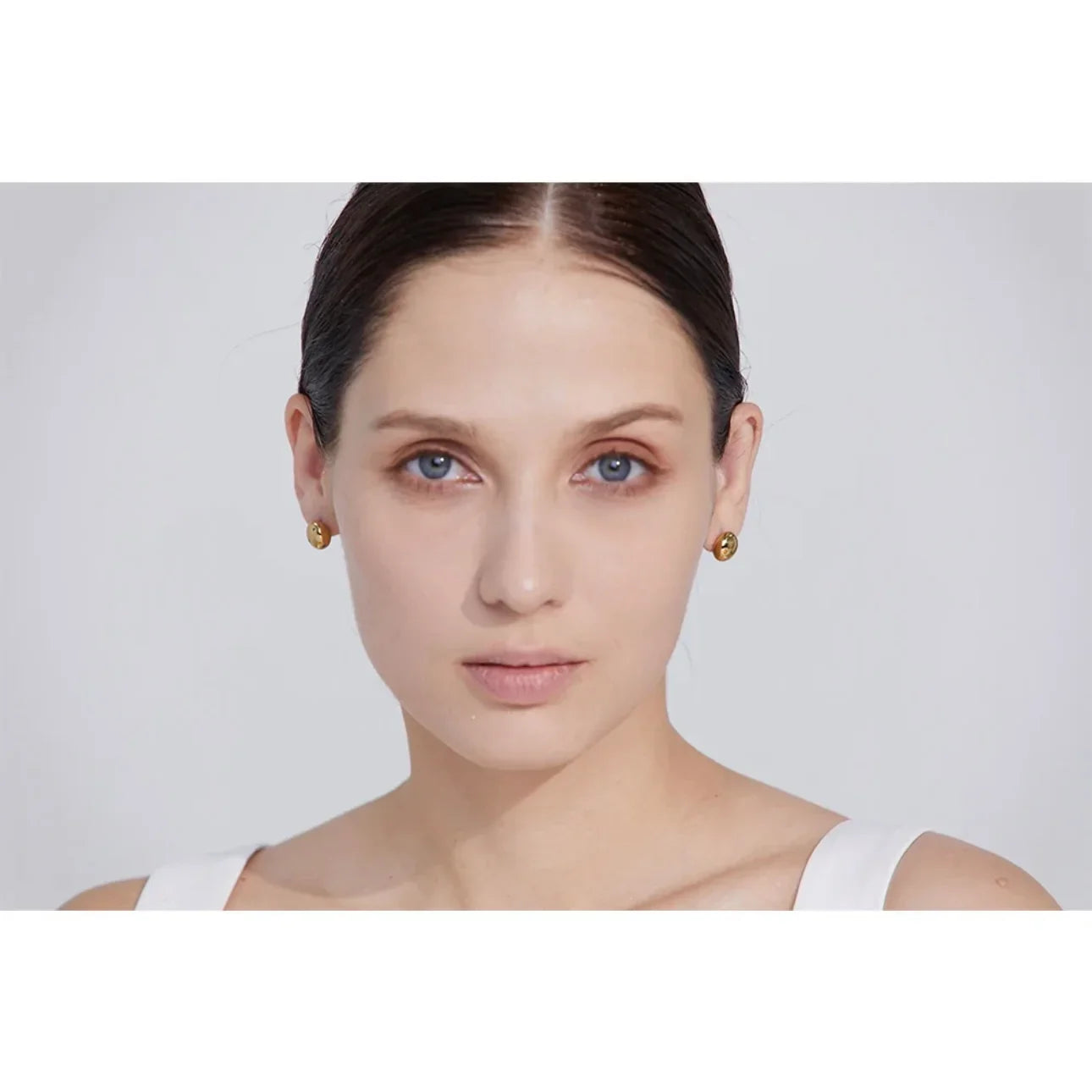 Woman wearing gold stud earrings against a plain light background