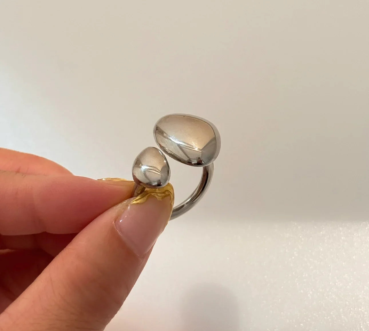 Hand holding a modern silver adjustable open ring with two polished pebble shapes