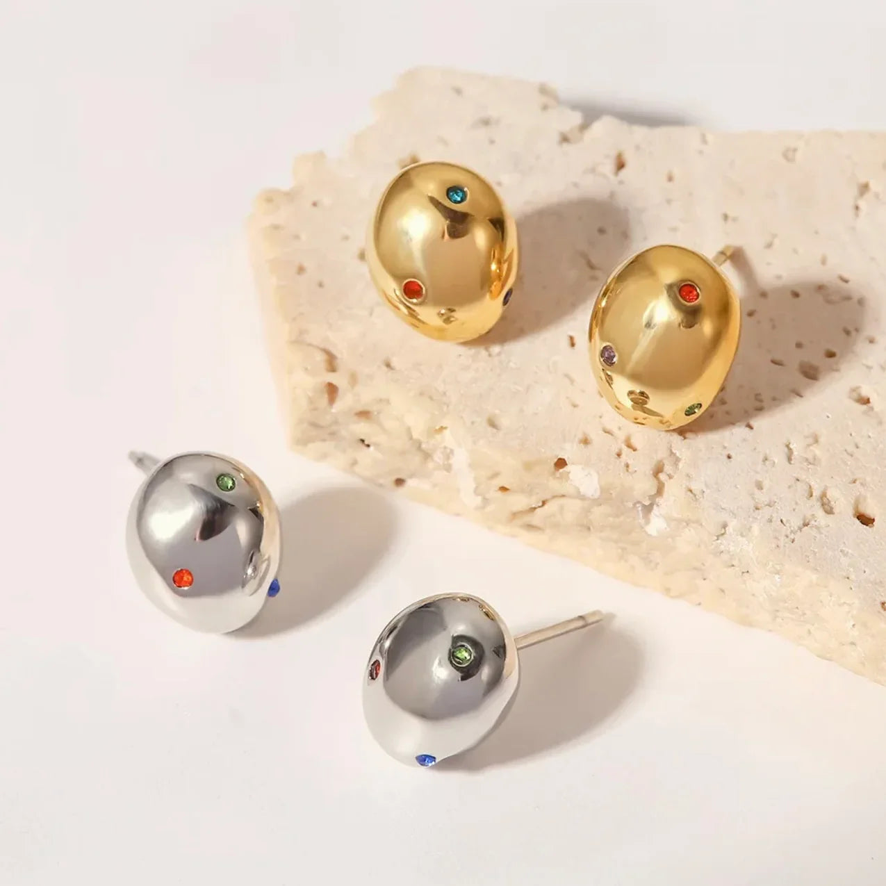 Gold and silver dome stud earrings with colorful gemstones on a stone background