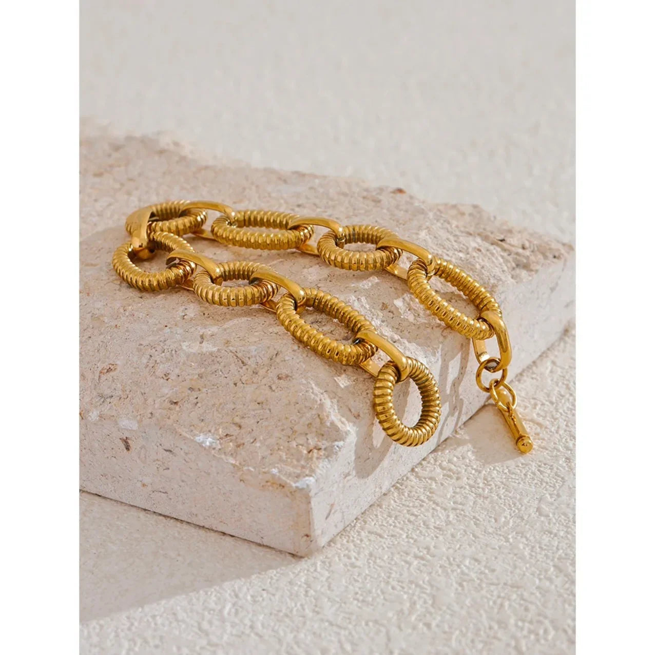 Textured gold chain bracelet with oval links on a beige stone surface
