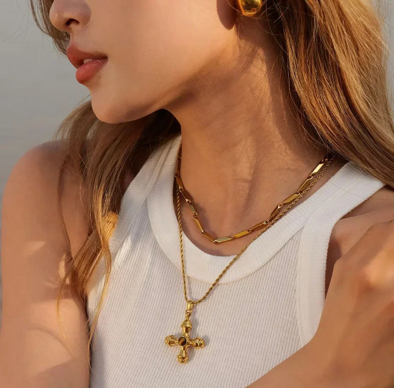 Woman wearing layered gold chain necklaces with cross pendant and gold earrings