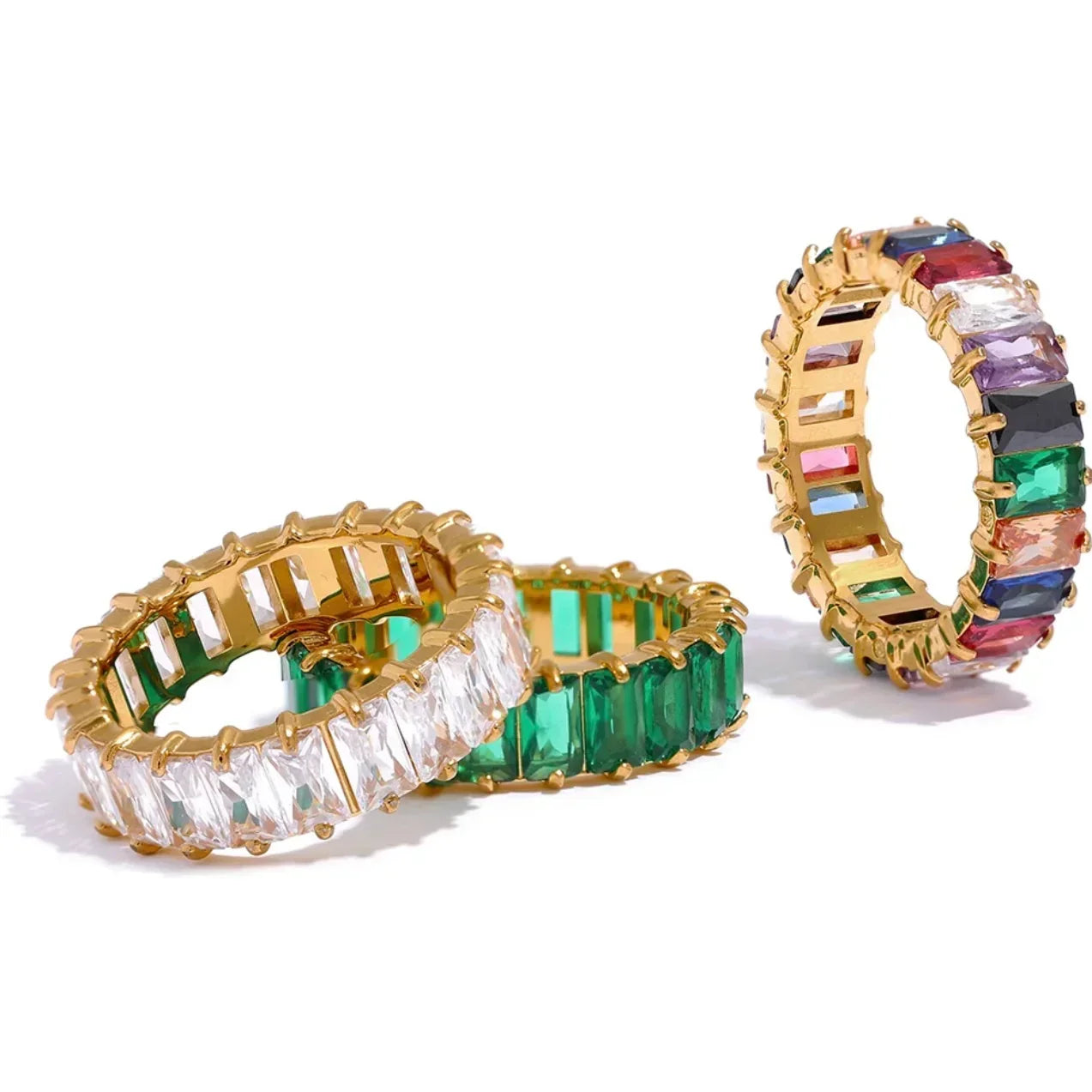 Three gold eternity bands with baguette-cut gems in clear, green, and multicolor settings