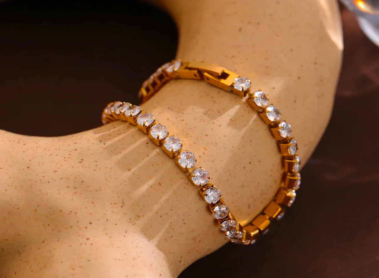 Gold tennis bracelet with round clear stones displayed on a beige mannequin hand