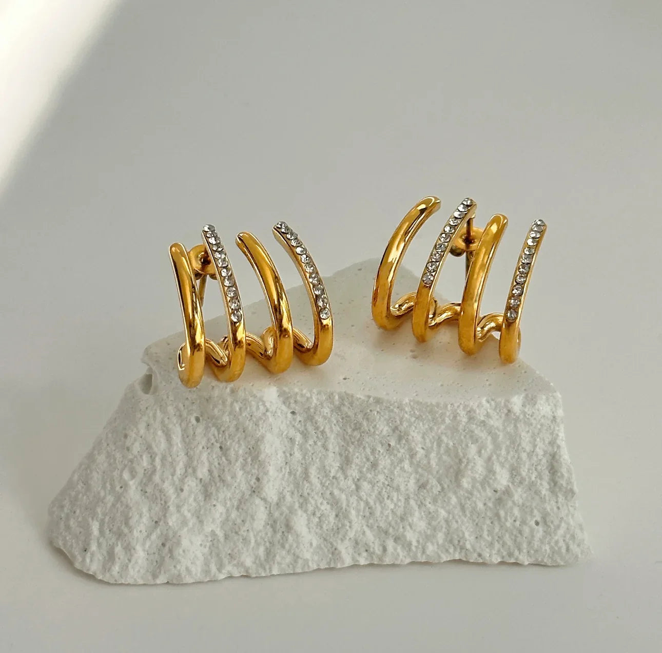 Gold triple hoop earrings with crystal accents displayed on textured white stone